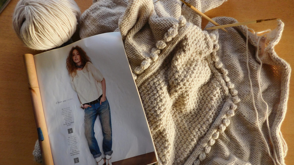Mon pull gris à noppes Phildar en cours de tricot avec le catalogue de modèles et la laine Katia Merino Aran.