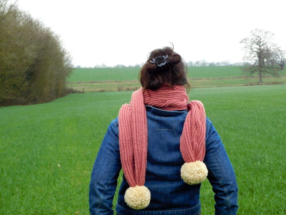 Ma grosse écharpe vieux rose avec ses énormes pompons crème tricotée main avec une torsade de côtes anglaises de dos.