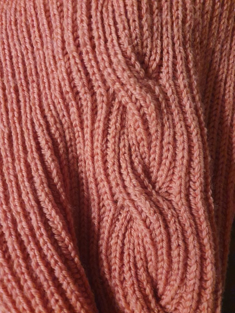 Ma grosse écharpe vieux rose avec ses énormes pompons crème tricotée main avec une torsade de côtes anglaises en gros plan sur le motif.